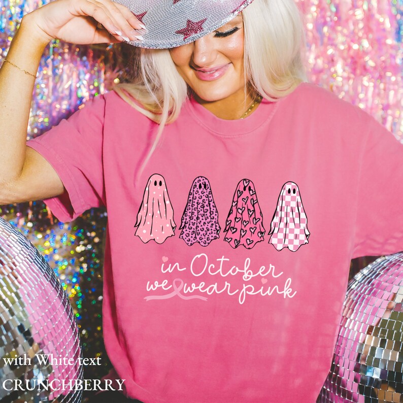 May include: Pink t-shirt with a graphic of four ghosts wearing different patterns. The ghosts are lined up horizontally. The text "in October we wear pink" is below the ghosts with a pink ribbon symbol.