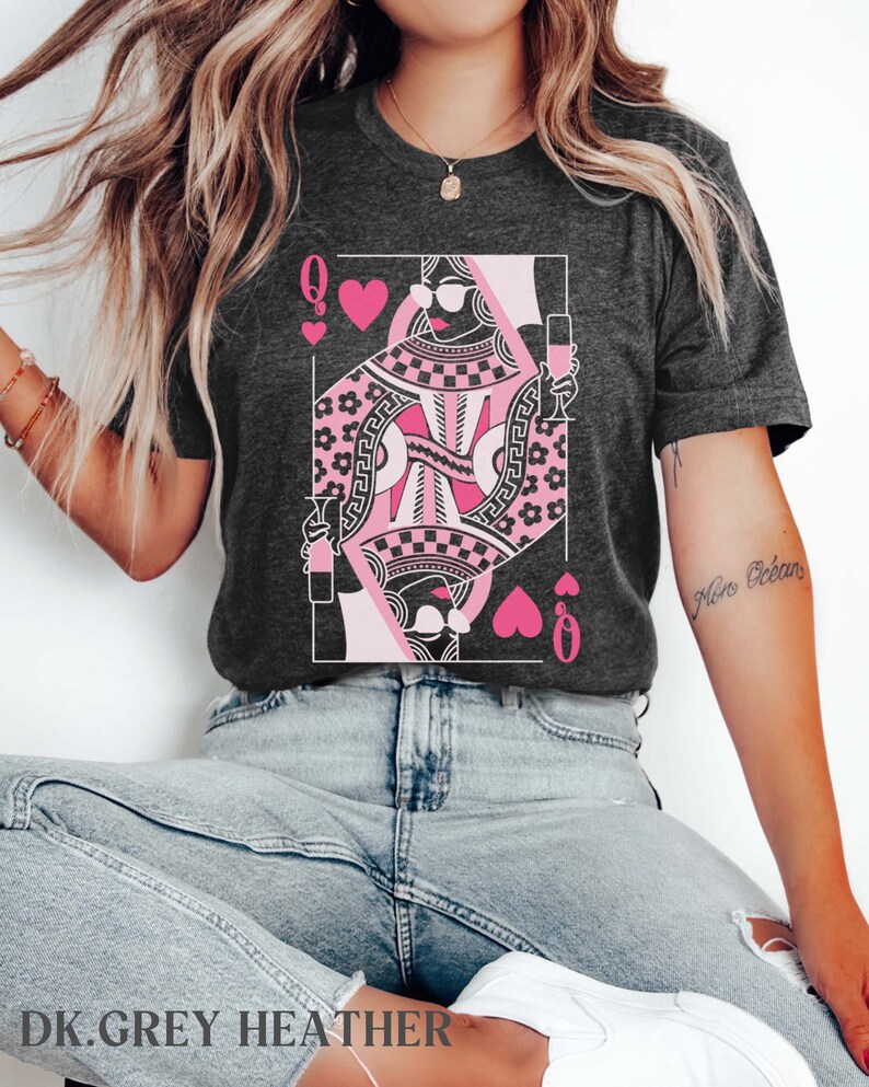 K&ouml;nnte beinhalten: Ein dunkelgraues Heather-T-Shirt mit einer pinkfarbenen und schwarzen Grafik der Herzdame aus Spielkarten. Die Dame tr&auml;gt eine Sonnenbrille und h&auml;lt ein Glas Wein in der Hand. Der Text "More Oceans" steht auf dem rechten &Auml;rmel des Shirts.