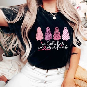 May include: Black t-shirt with a pink ribbon and the text "in October we wear pink". Four ghosts are printed on the shirt, each with a different pink pattern.