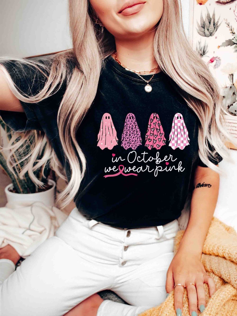 May include: Black t-shirt with a pink ribbon and the text "in October we wear pink". Four ghosts are printed on the shirt, each with a different pink pattern.