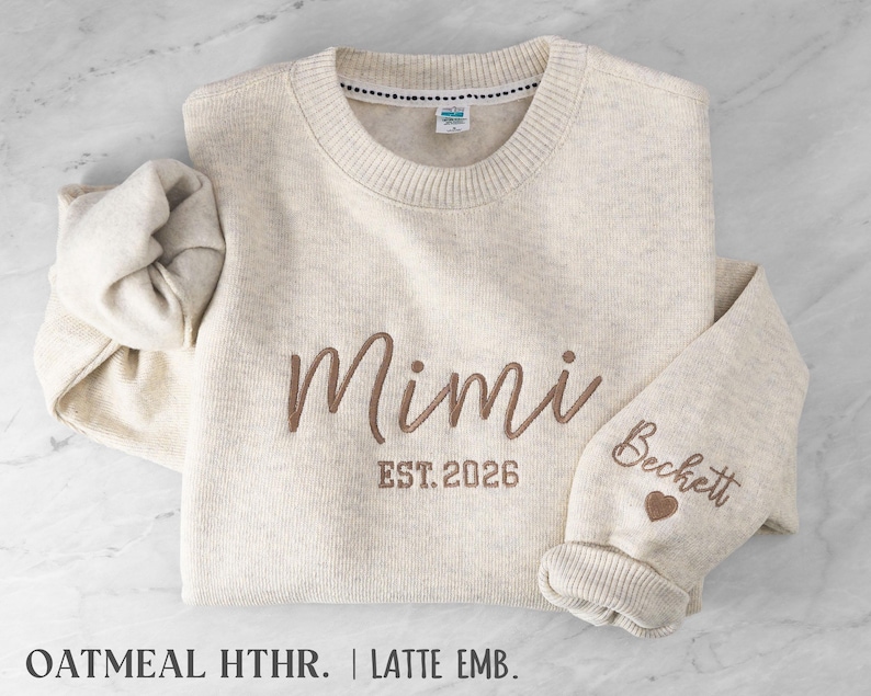 May include: An oatmeal heather crewneck sweatshirt featuring brown embroidery on the chest that reads Mimi EST. 2026. The sleeve is embroidered with the name Beckett and a small heart icon. The garment has a ribbed collar and cuffs.