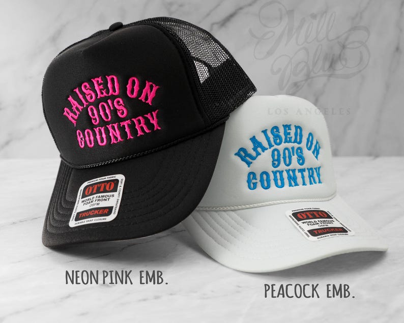May include: Two trucker hats, one black and one white, with the embroidered text "RAISED ON 90'S COUNTRY." The black hat has neon pink embroidery, and the white hat has peacock blue embroidery. Both hats have a mesh back and a curved brim.