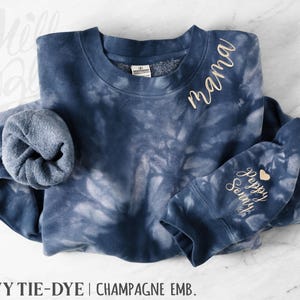 May include: Navy tie-dye sweatshirt with champagne embroidery. The word "mama" is embroidered on the upper chest. The sleeve cuff features the words "Poppy Sonny" and a heart. A comfortable, casual style sweatshirt.