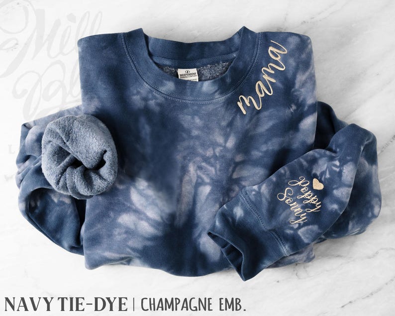May include: Navy tie-dye sweatshirt with champagne embroidery. The word "mama" is embroidered on the upper chest. The sleeve cuff features the words "Poppy Sonny" and a heart. A comfortable, casual style sweatshirt.