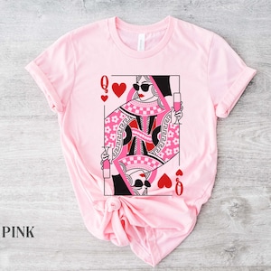 K&ouml;nnte beinhalten: Pinkes T-Shirt mit einem Grafikdruck einer Herzdame Spielkarte mit Sonnenbrille und einem Glas Champagner. Die Dame tr&auml;gt ein pinkfarbenes und schwarzes Karomuster.