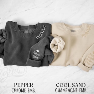 May include: Two crewneck sweatshirts, one dark grey and one beige, with embroidered text. The dark grey sweatshirt has "momma" on the collar and "Elliana Ethan" on the sleeve. The beige sweatshirt has "mama" and names on the sleeve.