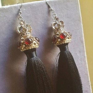May include: A pair of black tassel earrings with gold crown-shaped tops and red gemstone accents.