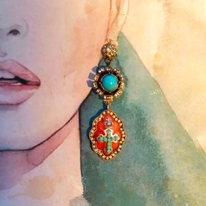 May include: A pair of dangle earrings featuring a turquoise stone and a cross pendant. The earrings are gold-toned and have an intricate design.