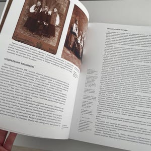 May include: A book open to a page with a black and white photo of a group of people. The text on the page is in Ukrainian and discusses the history of Ukrainian embroidery.