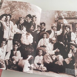 May include: A black and white vintage photograph of a large group of people, mostly women and children, standing in front of a building. The people are dressed in traditional clothing and some are holding flowers. The text "Grest Kholmova and a group of musicians performing folk songs, 1934.  A group of musicians from the village of Kholmovo, near the city of Orel, Russia.  The musicians are playing traditional Russian instruments, such as the balalaika, the domra, and the accordion." is printed at the bottom of the photo.