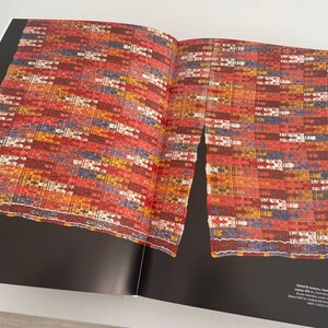 May include: A close-up of a colorful woven textile with red, blue, yellow, and white stripes. The textile is folded in half and appears to be a traditional garment.