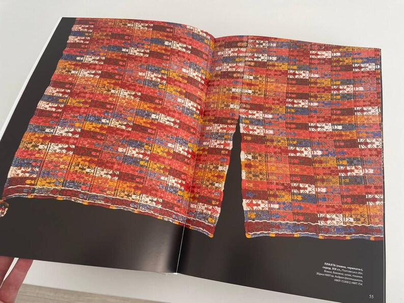 May include: A close-up of a colorful woven textile with red, blue, yellow, and white stripes. The textile is folded in half and appears to be a traditional garment.