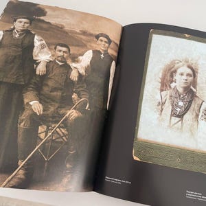 May include: A vintage black and white photo of a family in traditional clothing. The photo shows a woman in a long dress and a man in a suit. The photo is framed in a black frame with a green border.