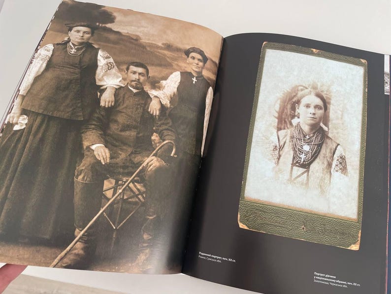 May include: A vintage black and white photo of a family in traditional clothing. The photo shows a woman in a long dress and a man in a suit. The photo is framed in a black frame with a green border.