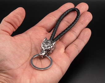 May include: A silver wolf head keychain with intricate details and a black leather strap.
