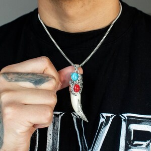 May include: A silver chain necklace with a white tooth pendant. The pendant has three stones: two turquoise and one red.