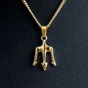 May include: A gold-tone necklace with a trident pendant. The necklace is on a black background.