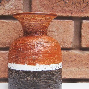 May include: A brown, white and black ceramic vase with a textured surface. The vase has a wide base and a narrow neck.