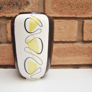 May include: A white ceramic vase with a black and yellow abstract design. The vase has a rounded shape and a narrow opening.