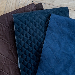 May include: Three pieces of quilted fabric in varying shades of brown and blue. The fabrics have a diamond pattern created by stitched lines. The textures appear soft and plush, suitable for upholstery or crafting projects.