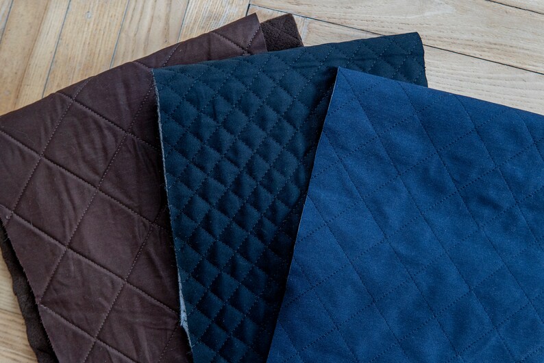 May include: Three pieces of quilted fabric in varying shades of brown and blue. The fabrics have a diamond pattern created by stitched lines. The textures appear soft and plush, suitable for upholstery or crafting projects.