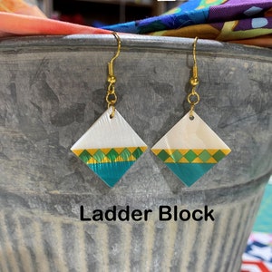 May include: A pair of gold dangle earrings with white, green, and gold diamond-shaped pendants. The earrings are labeled "Ladder Block".