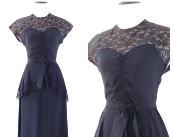 May include: A black vintage dress with a lace bodice and a tiered skirt. The dress has a sweetheart neckline and a bow at the waist.