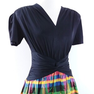 May include: A black short-sleeved dress with a V-neckline and a fitted bodice. The skirt is a colorful plaid pattern with red, yellow, green, blue, and pink.