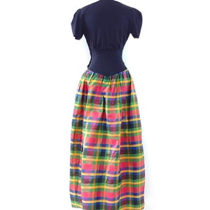 May include: A black short-sleeved top with a fitted bodice and a colorful plaid skirt. The skirt is a mix of red, yellow, green, and blue plaid.