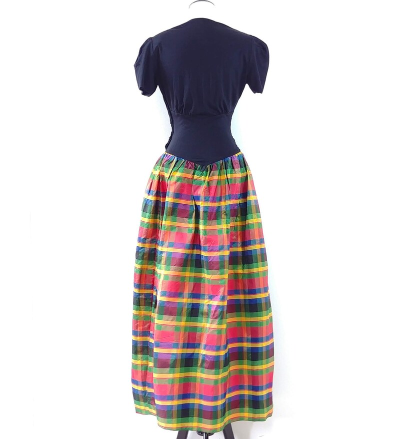 May include: A black short-sleeved top with a fitted bodice and a colorful plaid skirt. The skirt is a mix of red, yellow, green, and blue plaid.