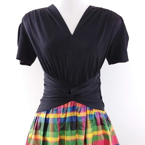 May include: A black short-sleeved dress with a V-neckline and a knotted waistband. The skirt is a colorful plaid pattern with red, yellow, green, blue, and purple.