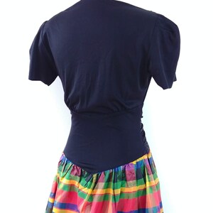 May include: A black short-sleeved dress with a fitted bodice and a colorful plaid skirt. The skirt is made of a shiny fabric and has a variety of colors, including red, green, yellow, and blue.