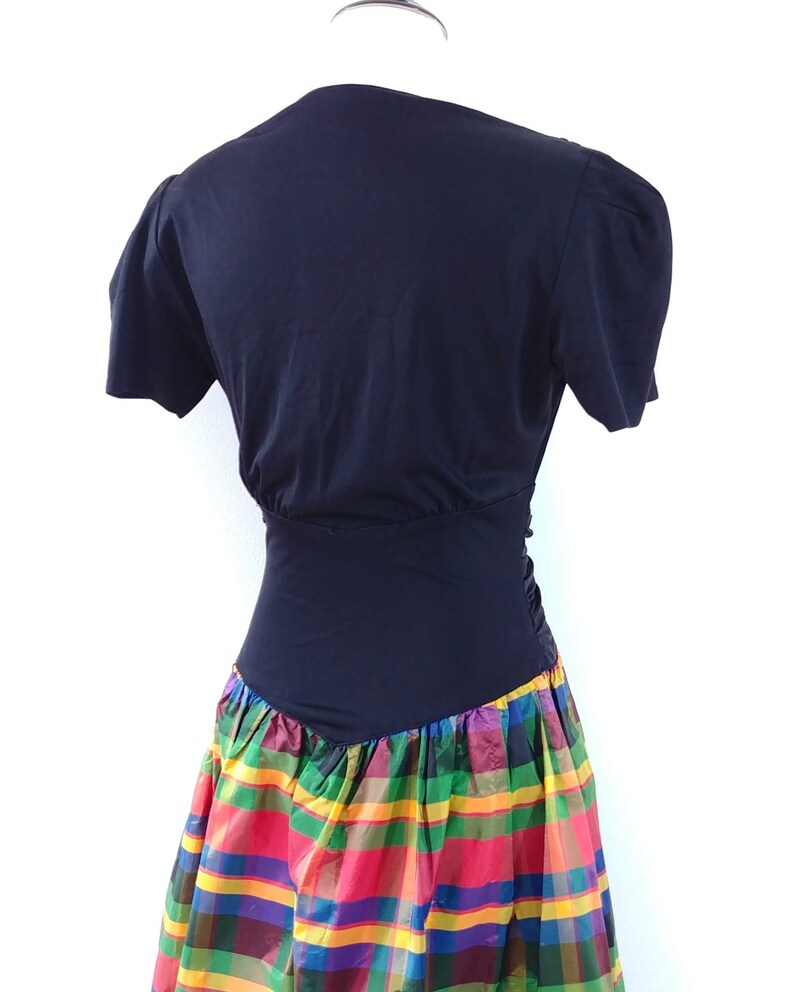 May include: A black short-sleeved dress with a fitted bodice and a colorful plaid skirt. The skirt is made of a shiny fabric and has a variety of colors, including red, green, yellow, and blue.