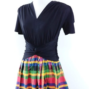 May include: A black short-sleeved dress with a V-neckline and a fitted bodice. The skirt is a colorful plaid pattern with red, yellow, green, blue, and purple hues.