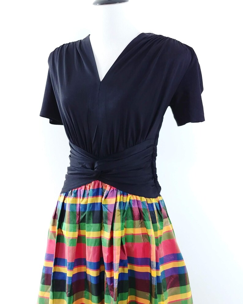 May include: A black short-sleeved dress with a V-neckline and a fitted bodice. The skirt is a colorful plaid pattern with red, yellow, green, blue, and purple hues.