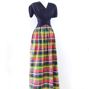 May include: A black short-sleeved top with a twist detail at the waist, paired with a long, colorful plaid skirt.