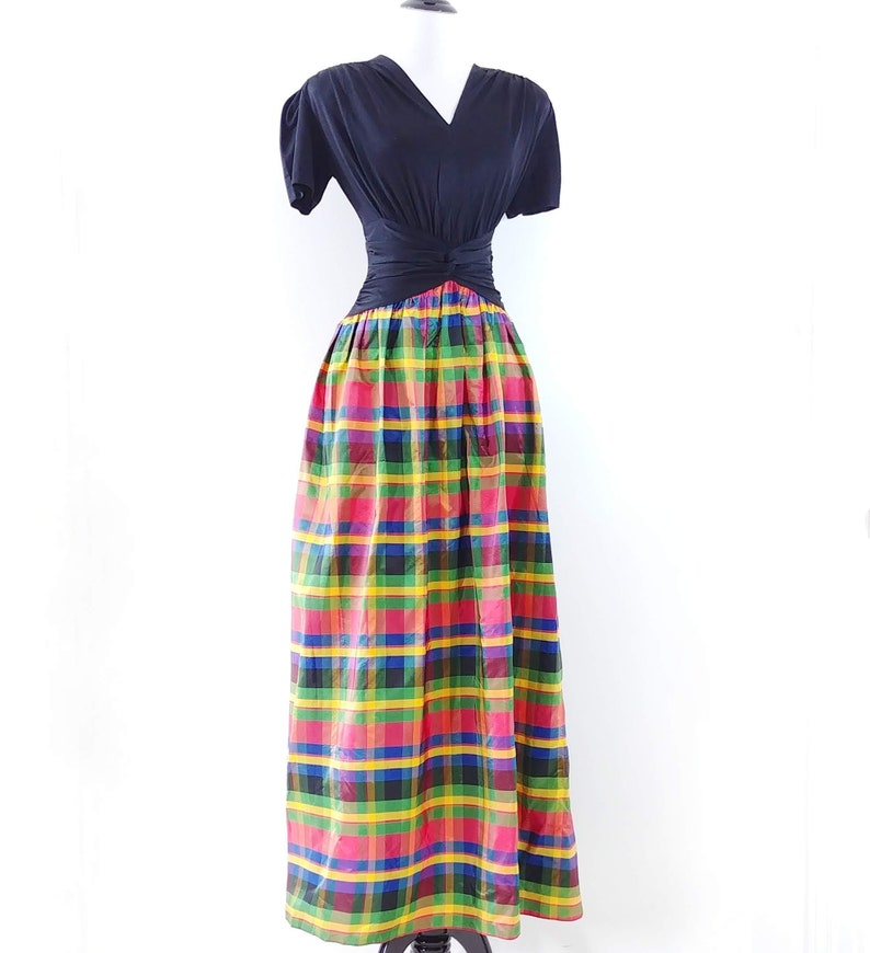 May include: A black short-sleeved top with a twist detail at the waist, paired with a long, colorful plaid skirt.
