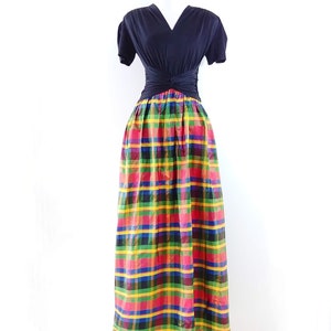 May include: A black short-sleeved top with a V-neckline and a knot at the waist, paired with a long, colorful plaid skirt. The skirt features a red, yellow, green, blue, and black plaid pattern.