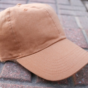 May include: A brown baseball cap with a curved brim. The cap is made of a soft, cotton fabric.