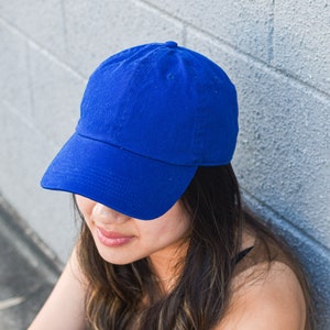 May include: A solid blue baseball cap with a curved brim. The cap is made of a soft fabric and has a classic six-panel design. The hat is a vibrant shade of blue and is suitable for casual wear.