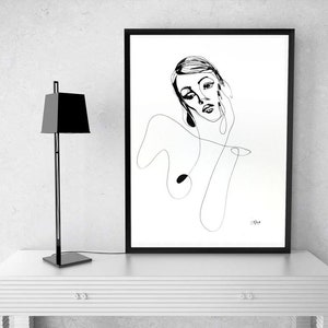 Może przedstawiać: Czarny obraz w ramie z minimalistycznym rysunkiem linii twarzy i g&oacute;rnej części ciała kobiety. Czarna, nowoczesna lampa stoi po lewej stronie grafiki na białym stole. Grafika to prosty, elegancki design.