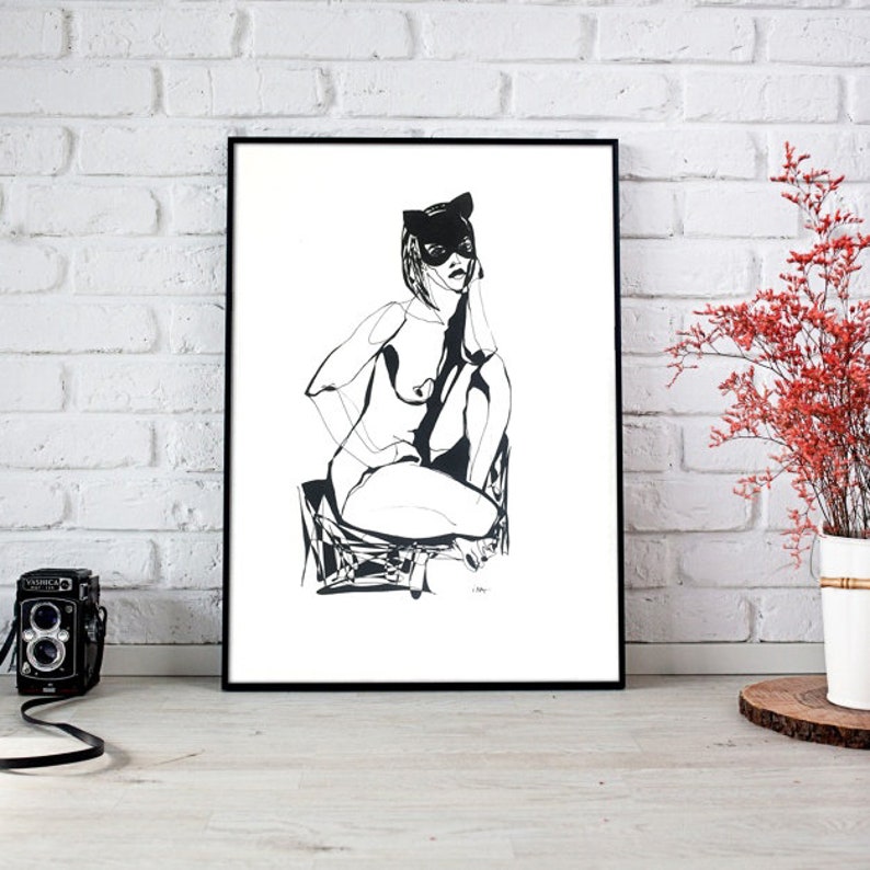 Puede incluir: Dibujo a tinta en blanco y negro de una persona con una m&aacute;scara de gato, sentada en una silla. La obra de arte est&aacute; enmarcada en un marco negro y se apoya contra una pared de ladrillos blancos. Una c&aacute;mara vintage y un jarr&oacute;n con flores rojas est&aacute;n en primer plano.