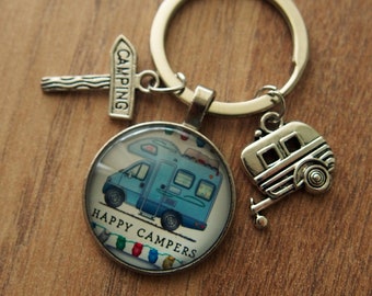 May include: A silver keychain with a blue camper van charm, a silver camper trailer charm, and a silver sign that says "Camping". The charm with the camper van has the words "Happy Campers" written on it.