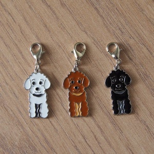 Può includere: Tre ciondoli a forma di cane con chiusure argentate. I ciondoli sono bianchi, marroni e neri, ciascuno con un collare nero. I ciondoli sono probabilmente per un braccialetto o una collana e sono fatti di metallo.