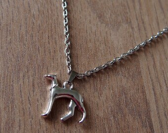 Puede incluir: Un collar de cadena de plata con un colgante de perro de plata. El perro está de pie sobre sus cuatro patas y tiene un diseño elegante y moderno.