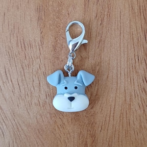 Op de afbeelding: Een zilveren bedel met een grijs en wit miniatuur schnauzer gezicht.