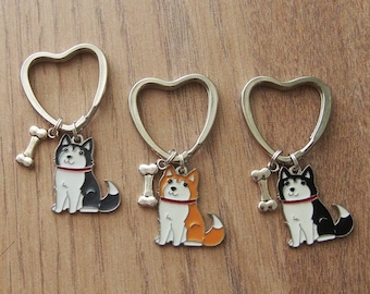 May include: Three heart-shaped keychains with dog charms. Each charm features a different dog breed: a black and white husky, an orange and white husky, and a black and white husky. Each charm also has a bone attached.