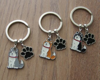 May include: Three silver keychains with dog charms. Each keychain features a different colored husky dog charm with a black paw print charm. The husky dogs are gray, orange, and black.