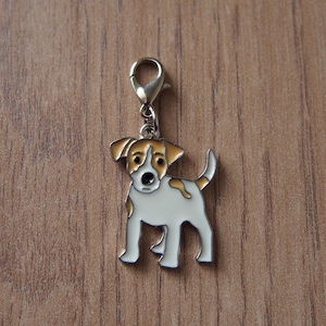 Op de afbeelding: Een zilveren bedel met een witte en bruine Jack Russell Terrier met zwarte ogen. De bedel heeft een zilveren lus aan de bovenkant om aan een armband of ketting te bevestigen.