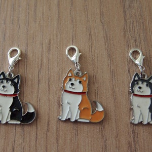 May include: Three metal charms featuring cartoon husky dogs. The dogs are sitting and have red collars. The charms are silver and have a clip on the top. The dogs are black and white, orange and white, and black and white.
